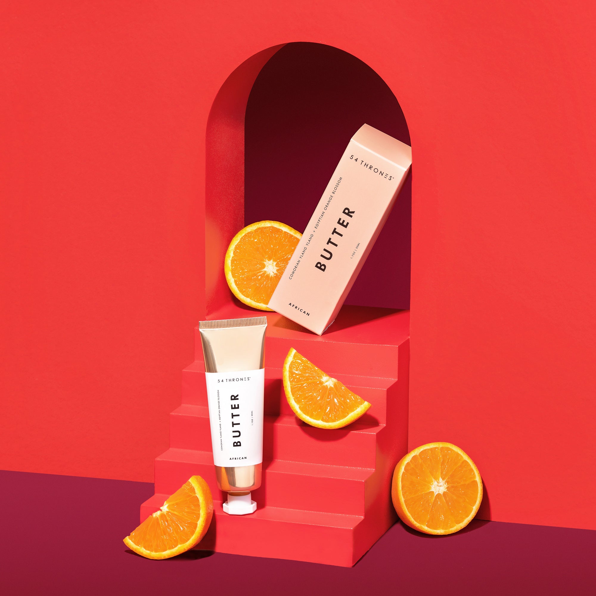 Gold Beauty Butter tube & box propped against a red background and surrounded by sliced oranges | 54 Thrones